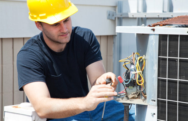 A technician in a yellow hardhat repairing an HVAC unit